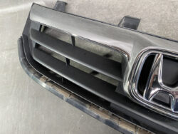 Front grille of a Honda vehicle with black horizontal slats and a chrome surround featuring the Honda badge on the right side of the frame.