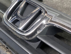 Close-up of a shiny chrome car interior trim piece with a partially visible Honda emblem, showing wear and chipped edges around the edge of the panel.