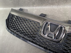 Close-up of a Honda front grille with chrome emblem on a honeycomb mesh