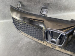 Front view of a black car grille with the Honda emblem, showing the bumper area and lower grille in a workshop setting.