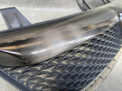 Close-up of a black car's front bumper and honeycomb grille with dust and light scratches.