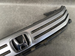 Front grille of a Honda car featuring the chrome H emblem and three horizontal slats.