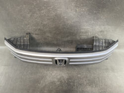 Front bumper cover for Honda, gray with horizontal chrome accents and emblem in the center, viewed from the front in a workshop setting.
