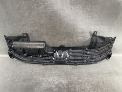 Black plastic front bumper/grille assembly with air intake vents laid flat on a textured surface, automotive part for a car front end