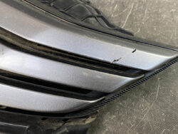 Scratched silver car bumper with a small gouge along the vent area, near the wheel arch.