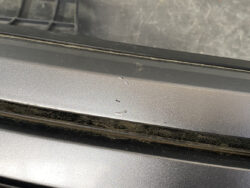 Close-up of a silver car door trim with several small paint chips and dirt along the seam.