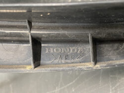 Close-up of a black plastic car part with 'HONDA' and 'AES' markings stamped in the molded surface.