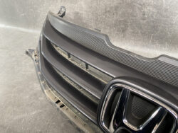 Close-up of a black car front grille with a chrome Honda emblem on the right side of the image.