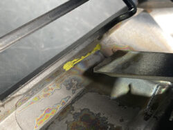 Close-up of a corroded metal interior with rainbow oxide patterns and a small yellow paint smear near a metal edge.