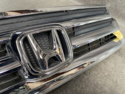 Close-up of the Honda front grille and emblem on a dark vehicle, with yellow tape visible on the right side.