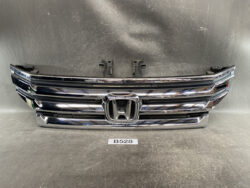 Chrome Honda front grille with classic 'H' emblem, resting on a workshop surface.