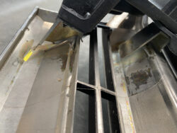 Close-up of a rusting metal framework with corroded panels and a yellow tag, suggesting maintenance access in an industrial machine.