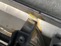 Close-up of metal piece with rainbow heat discoloration near a black plastic clamp and screw inching along a joint.