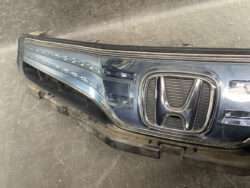 Front bumper and chrome Honda grille, blue car panel removed and resting on a workshop floor