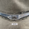 Chrome Honda front grille and bumper assembly laid on a workshop floor, emblem centered