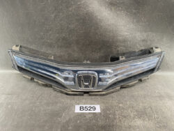 Chrome Honda front grille and bumper assembly laid on a workshop floor, emblem centered