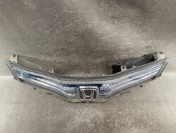 Front view of a detached Honda front grille and bumper assembly with emblem in the center on a scratched floor surface