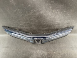Chrome Honda front grille with emblem centered, laid on a dark workshop floor surface