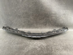 Chrome car bumper trim piece with mounting clips, curved along its length against a scratched surface
