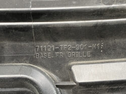 Close-up of a black plastic car part with stamped part number 71121-TF2-901-M1 and the text 'BASE FR GRILLE'.