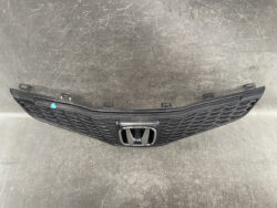 Front grille of a Honda car with a chrome emblem in the center, resting on a dark surface.
