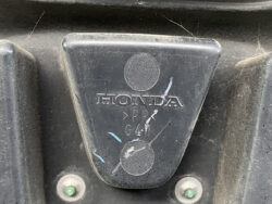 Close-up of a black plastic Honda component with embossed HONDA text and markings, dusty surface visible around it.