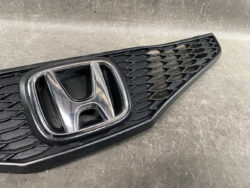 Close-up of a black honeycomb car grille featuring a chrome Honda emblem in the center.