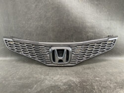 Front grille of a Honda car featuring a prominent chrome H emblem and a honeycomb mesh pattern