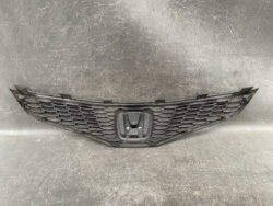 Front view of a black car grille featuring a central Honda emblem and honeycomb mesh pattern in a V-shaped design.