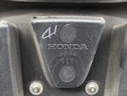 Close-up of a black Honda plastic part with embossed 'HONDA' and material code, two silver screws visible below.