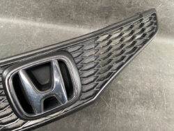 Close-up of a Honda front grille with a chrome H emblem on a dark honeycomb background.