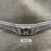 Front Honda car grille with honeycomb mesh and central logo, shown as a spare part on a workshop surface HONDA FIT JAZZ GE6 GE7 Genuine Radiator Grille 71121-TF0-00 » JDM-PARTS NZ