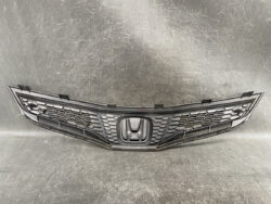 Front grille of a Honda vehicle with a honeycomb mesh and central emblem in the middle of the bumper area.