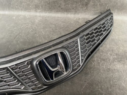 Close-up of a black car front grille with a chrome Honda emblem in the center, featuring a honeycomb mesh pattern.
