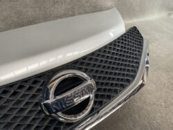 Close-up of Nissan emblem on the front grille of a car with a chrome border and diamond-pattern grille. It reads NISSAN in the center.