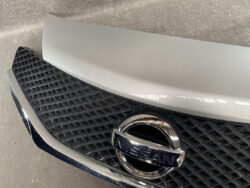 Close-up of the front end of a silver Nissan car, showing the grille and chrome emblem.