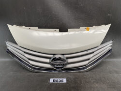 Front view of a Nissan car grille with chrome slats and circular Nissan badge, plus a light-colored hood panel resting above it.