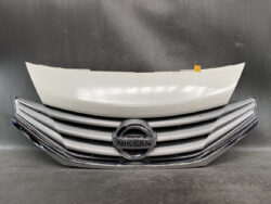 Front view of a Nissan car grille and bumper with a detached white hood piece resting above the grille, set on a dark surface.