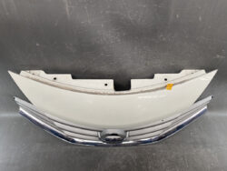 Gray curved bumper cover resting above a chrome Nissan grille with emblem in the center on a dark surface
