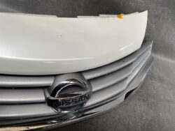 Close-up of a Nissan front grille and chrome emblem on a silver car, with a small dent and scuff on the hood edge.