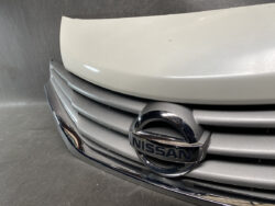 Front grille of a Nissan car featuring the chrome Nissan emblem on a silver bumper.