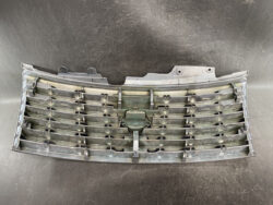Plastic car grille with many horizontal slats and central emblem area, lying on a dark workbench.