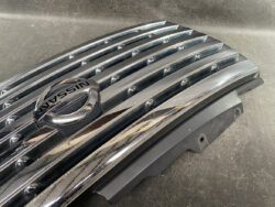 Close-up of a chrome Nissan badge on a ribbed grille panel.