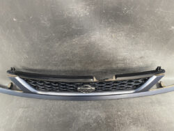 Front grille assembly from a Nissan car with emblem, placed on a scratched surface.
