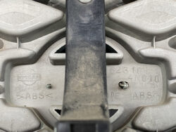 Close-up of a Nissan ABS brake hub with embossed Nissan logo and part numbers, showing a dusty gray plastic/metal assembly.