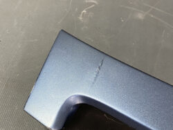Close-up of a blue metal surface with a small crack along a curved edge.