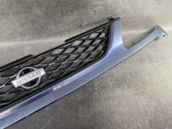 Nissan front grille piece with a blue body panel and honeycomb mesh, featuring the Nissan emblem in the center.