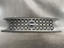 Front grille from a Nissan car with hexagonal honeycomb mesh and centered Nissan emblem.