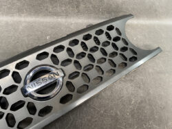Nissan front grille with a hexagonal mesh pattern and chrome Nissan emblem in the center, laid on a scratched surface