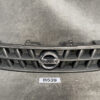 Nissan front grille with circular chrome emblem, black plastic slats, on a textured gray surface. NISSAN CUBE Z11 Genuine Radiator Grille 62310-4V70A » JDM-PARTS NZ